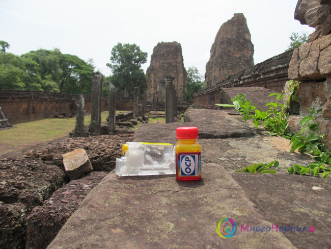 Чернила OCP и нано-картридж на фоне храма Пре Руп храмового комплекса Ангкор Ват в Камбодже